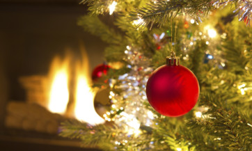 Bright red Christmas ornament hanging on Xmas Tree with fire place in background Bright red Christmas ornament hanging on Xmas Tree with fire place in background